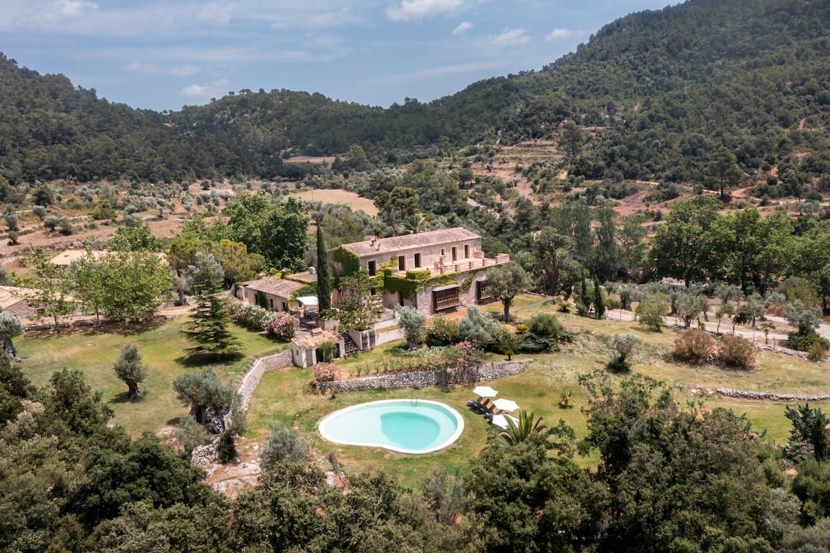 Die Finca Honor Vell von oben: Steinhaus mit Efeu, Garten und Pool inmitten von Olivenhainen und bewaldeten Hängen